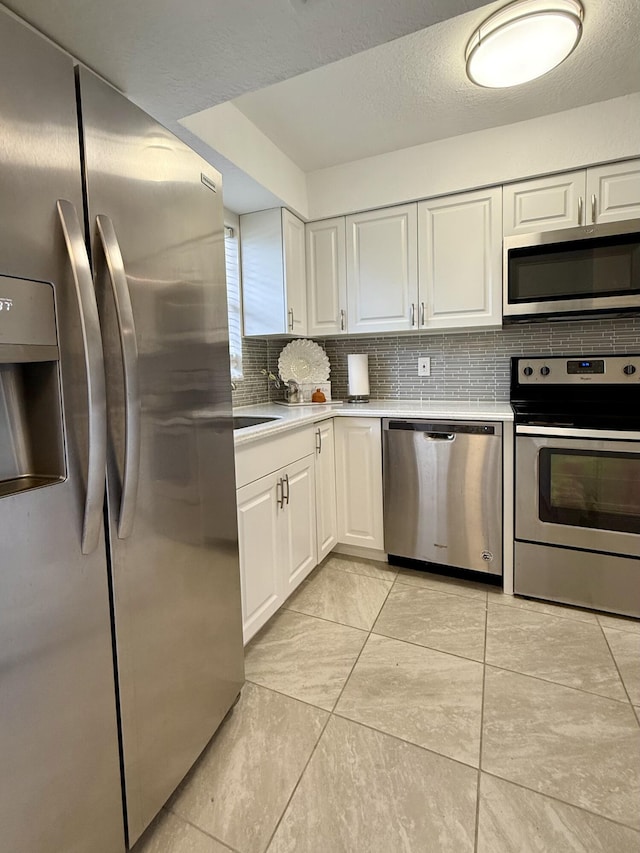 kitchen featuring tasteful backsplash, white cabinetry, light tile patterned flooring, and stainless steel appliances