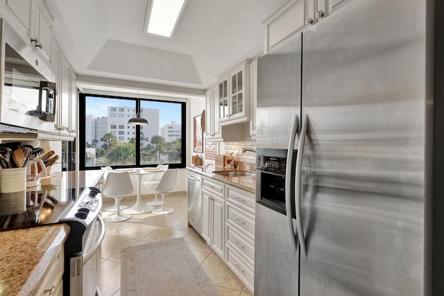 kitchen featuring light stone countertops, stainless steel appliances, pendant lighting, white cabinets, and lofted ceiling