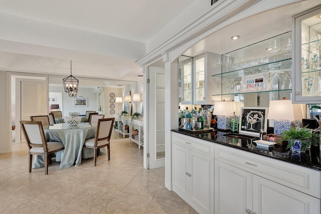 bar featuring dark stone counters, sink, hanging light fixtures, light tile patterned floors, and white cabinetry