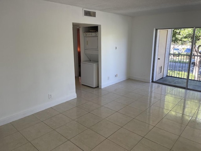 tiled spare room with a textured ceiling and stacked washer and clothes dryer