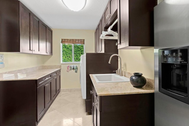 kitchen featuring sink, light stone counters, stainless steel refrigerator with ice dispenser, dark brown cabinets, and light tile patterned floors