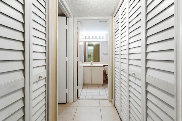 hall featuring light tile patterned floors, sink, and a textured ceiling