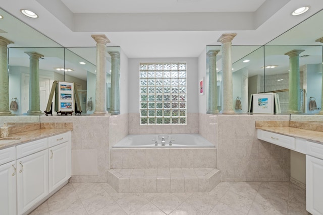 bathroom with tile patterned flooring, vanity, tiled bath, and ornate columns