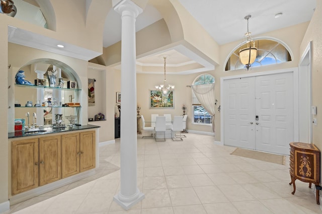 tiled foyer featuring decorative columns, an inviting chandelier, ornamental molding, and sink