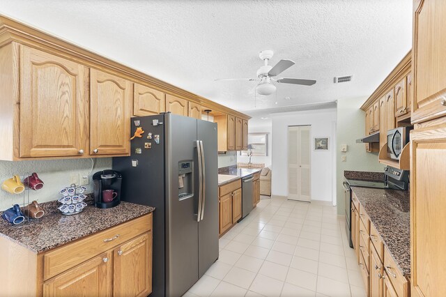 kitchen featuring appliances with stainless steel finishes, a textured ceiling, dark stone counters, and light tile patterned flooring