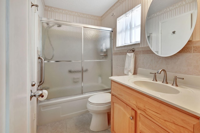 full bathroom featuring tile patterned floors, vanity, tile walls, enclosed tub / shower combo, and toilet