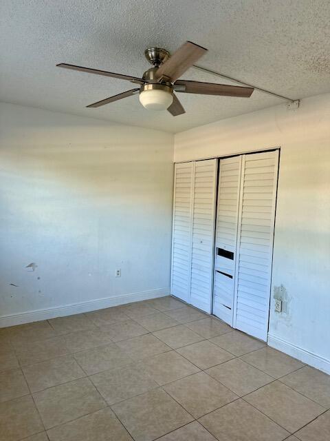 unfurnished bedroom featuring ceiling fan, light tile patterned floors, a textured ceiling, and a closet