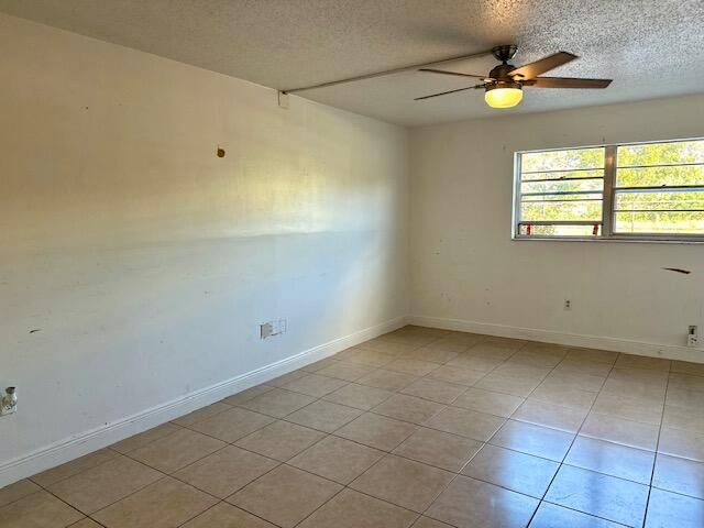 tiled empty room with ceiling fan and a textured ceiling