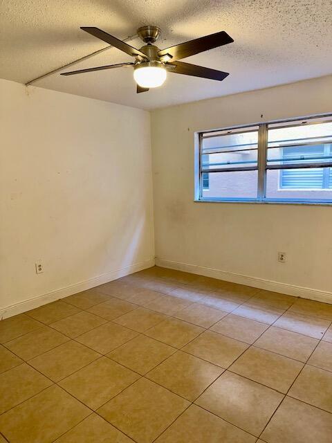 tiled empty room with ceiling fan and a textured ceiling