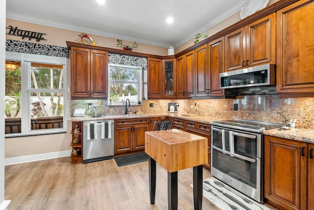 kitchen featuring sink, light hardwood / wood-style flooring, ornamental molding, light stone counters, and stainless steel appliances