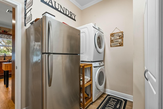 clothes washing area featuring light hardwood / wood-style flooring, stacked washer / drying machine, and ornamental molding