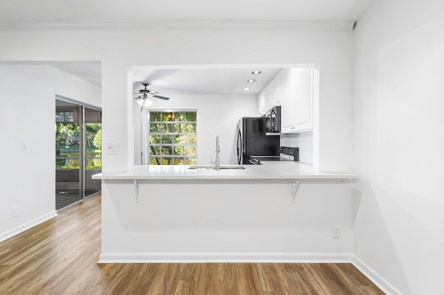 kitchen with kitchen peninsula, white cabinets, hardwood / wood-style flooring, and black appliances