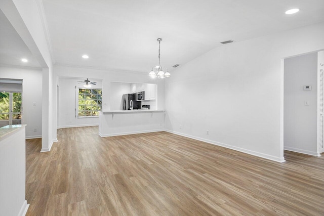 unfurnished living room with ceiling fan with notable chandelier, light hardwood / wood-style flooring, and a wealth of natural light