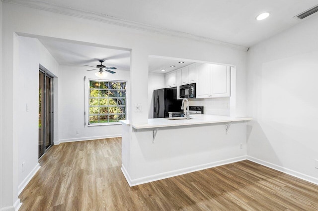 kitchen featuring black appliances, a kitchen breakfast bar, kitchen peninsula, light hardwood / wood-style flooring, and white cabinetry