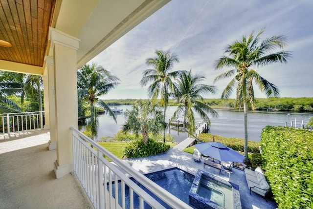 balcony with an in ground hot tub and a water view