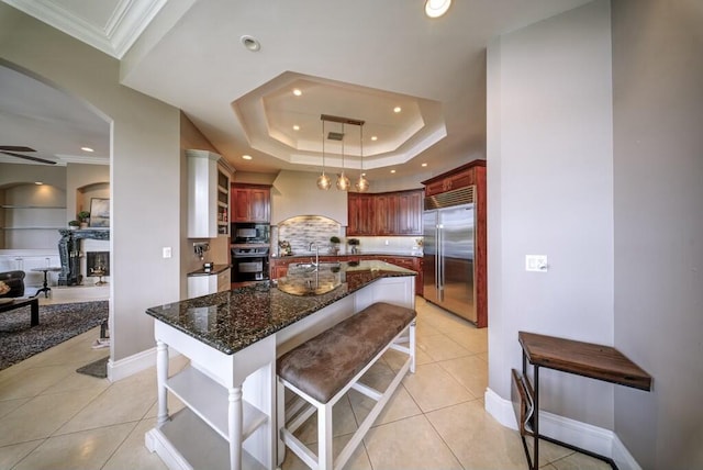 kitchen featuring hanging light fixtures, black appliances, light tile patterned flooring, a raised ceiling, and dark stone counters