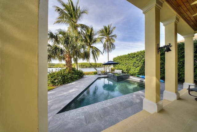 view of pool featuring an in ground hot tub, a water view, and a patio