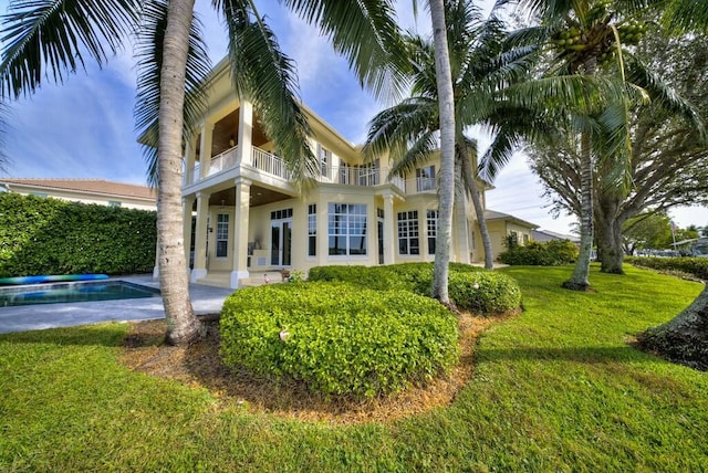 rear view of property with a balcony, a fenced in pool, and a lawn