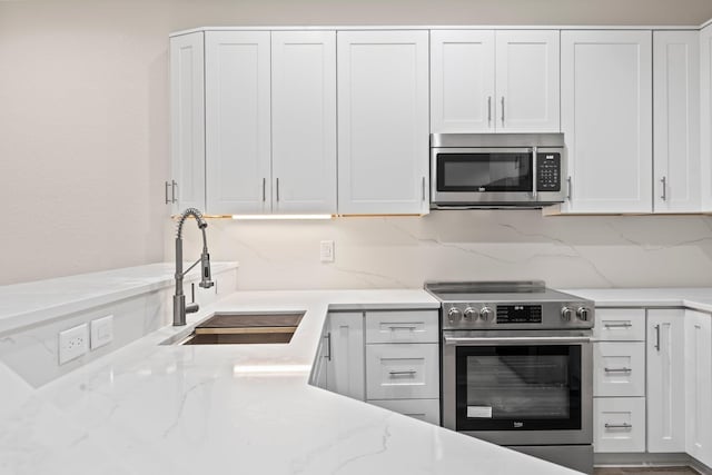 kitchen with light stone counters, sink, white cabinets, and appliances with stainless steel finishes