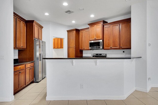 kitchen with kitchen peninsula, stainless steel appliances, a breakfast bar area, and light tile patterned flooring