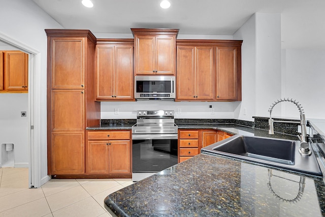 kitchen with light tile patterned floors, stainless steel appliances, dark stone counters, and sink