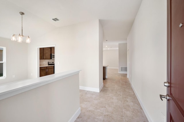 hallway featuring a chandelier, light tile patterned floors, and vaulted ceiling