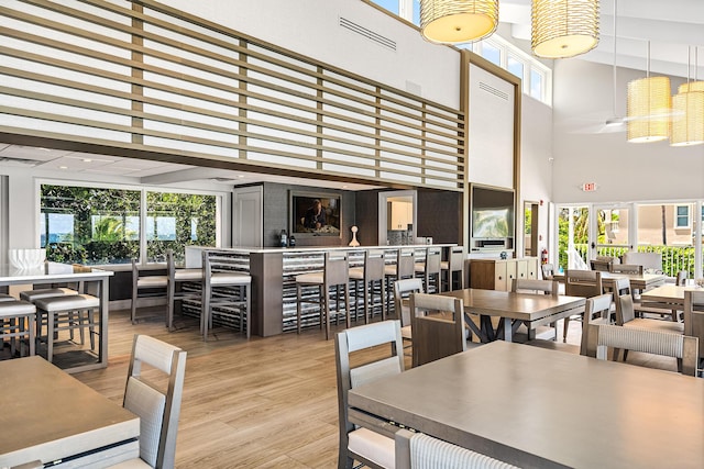 dining space featuring visible vents, wood finished floors, a towering ceiling, and a wealth of natural light