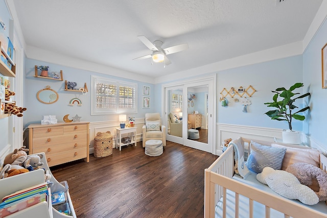 bedroom featuring a textured ceiling, ceiling fan, dark wood-type flooring, and a crib