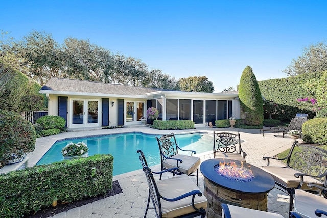 view of pool featuring a sunroom, a patio area, an outdoor fire pit, and french doors