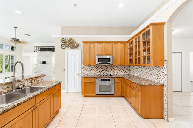 kitchen with appliances with stainless steel finishes, light stone counters, ceiling fan, sink, and light tile patterned floors