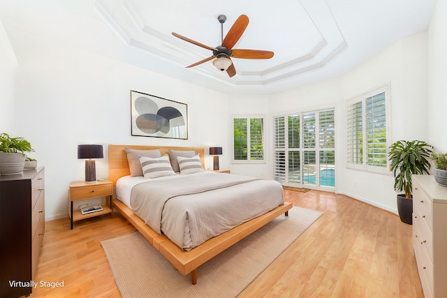 bedroom with ceiling fan, access to exterior, light wood-type flooring, ornamental molding, and a tray ceiling