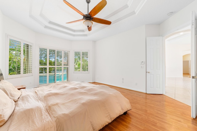 bedroom featuring ceiling fan, wood-type flooring, and a tray ceiling