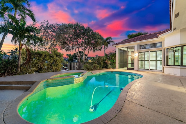 pool at dusk featuring an in ground hot tub, a patio, and a sunroom