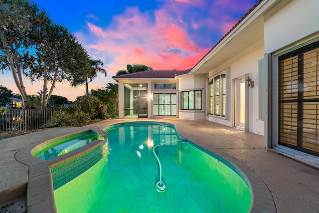 pool at dusk with a sunroom and an in ground hot tub