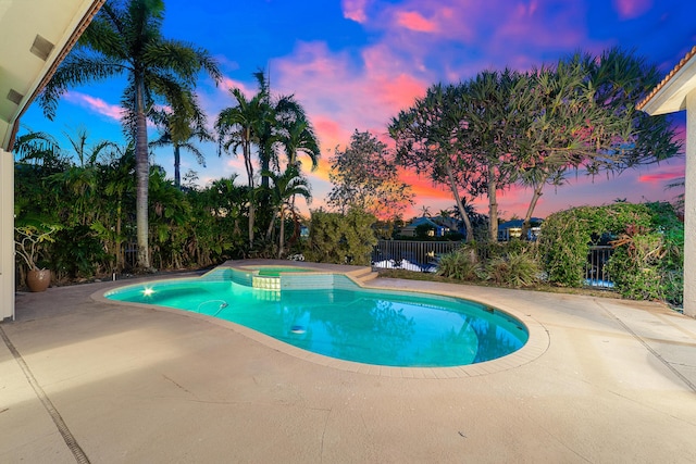 pool at dusk featuring an in ground hot tub and a patio