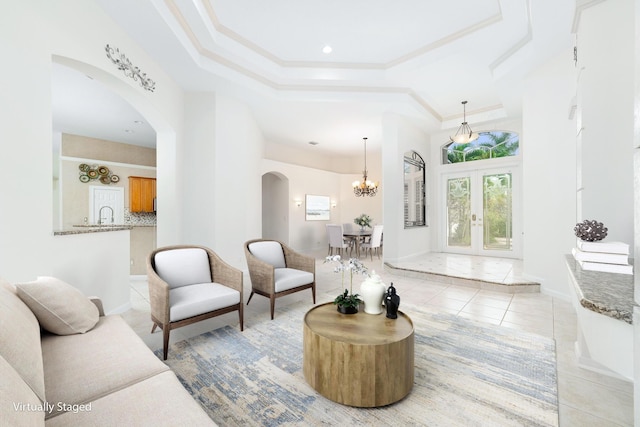 tiled living room featuring french doors, ornamental molding, a raised ceiling, sink, and a notable chandelier