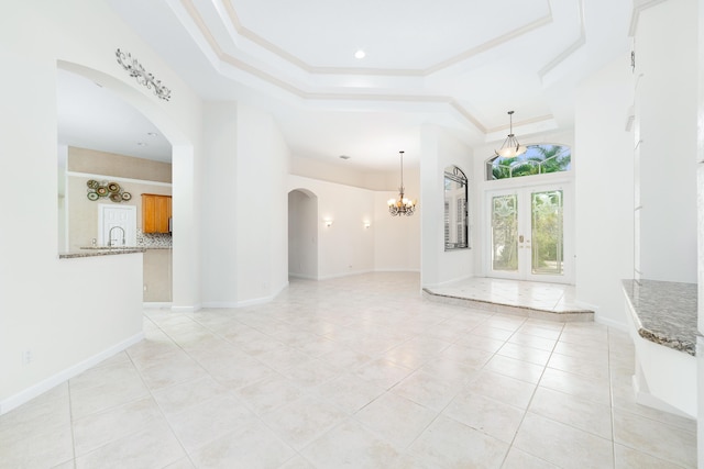 unfurnished living room featuring french doors, a tray ceiling, an inviting chandelier, and ornamental molding