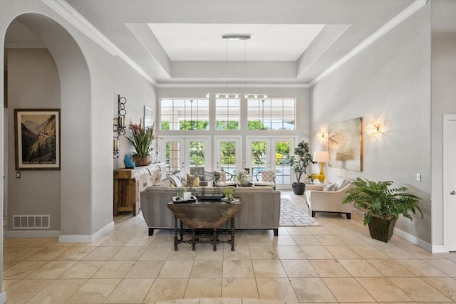 tiled living room with french doors, a towering ceiling, a raised ceiling, and ornamental molding