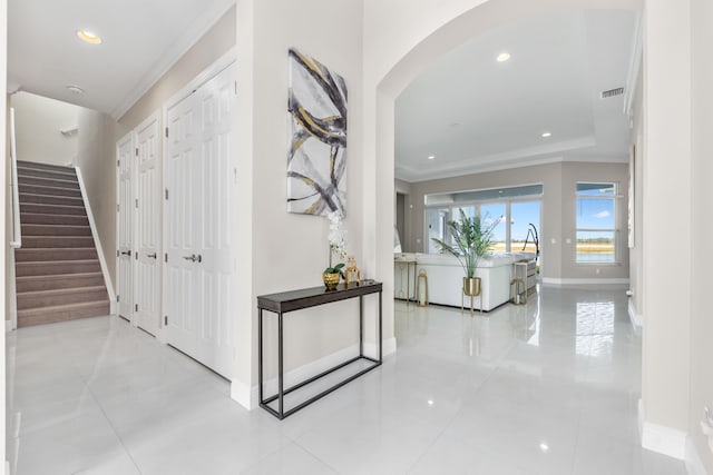 corridor featuring light tile patterned floors, a tray ceiling, and crown molding