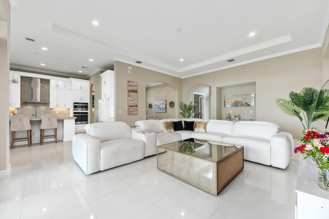 living room featuring light tile patterned floors, crown molding, and a tray ceiling