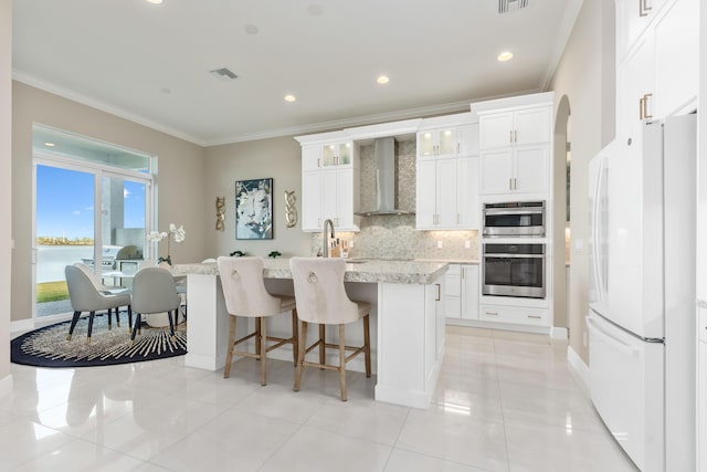 kitchen featuring white cabinetry, wall chimney range hood, white refrigerator, an island with sink, and a water view