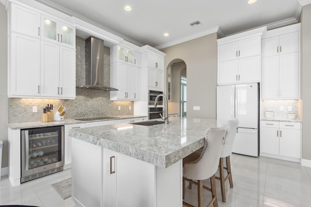 kitchen with a kitchen island with sink, wall chimney range hood, wine cooler, white fridge, and white cabinetry