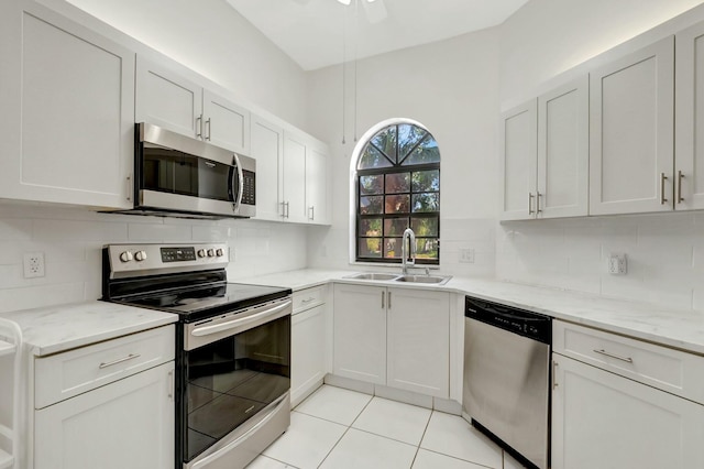 kitchen with light stone counters, light tile patterned flooring, a sink, stainless steel appliances, and backsplash