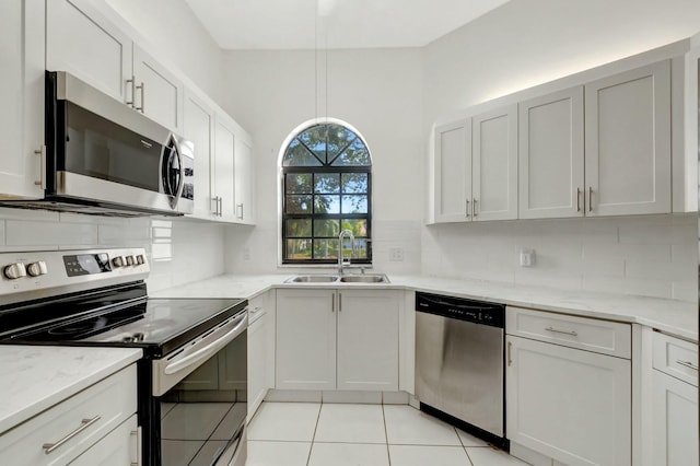 kitchen with a sink, stainless steel appliances, light stone countertops, and decorative backsplash