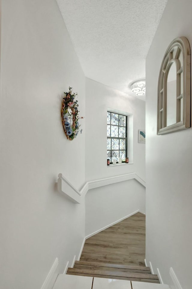 stairway with baseboards, a textured ceiling, and wood finished floors