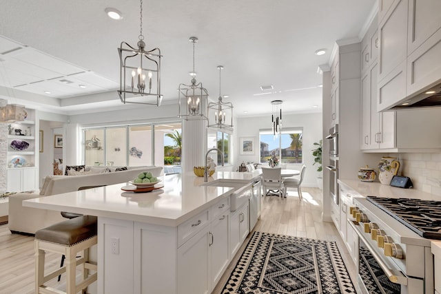 kitchen featuring sink, hanging light fixtures, gas range oven, an island with sink, and light hardwood / wood-style floors