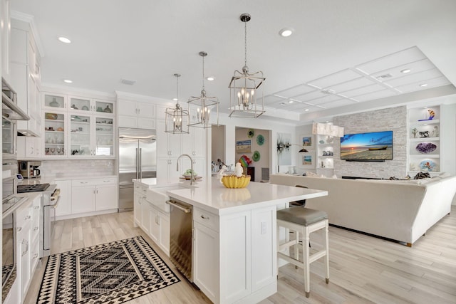 kitchen with a center island with sink, white cabinets, sink, light hardwood / wood-style flooring, and premium appliances