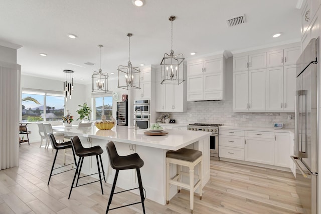 kitchen with a large island with sink, high quality appliances, white cabinets, and hanging light fixtures