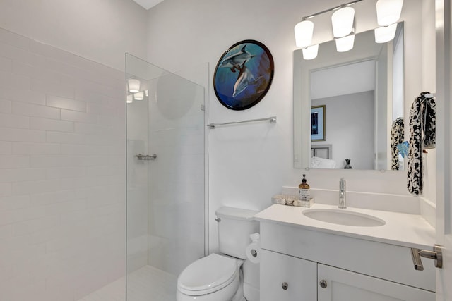 bathroom with toilet, a tile shower, and vanity