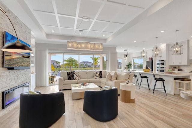 living room featuring a stone fireplace, light wood-type flooring, and coffered ceiling